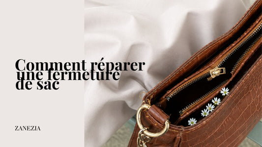 Sac à main marron effet croco avec fermeture éclair défectueuse, posé sur une chaise aux côtés de petites fleurs blanches. La tirette est bloquée au milieu tandis que les deux côtés de la fermeture restent ouverts.