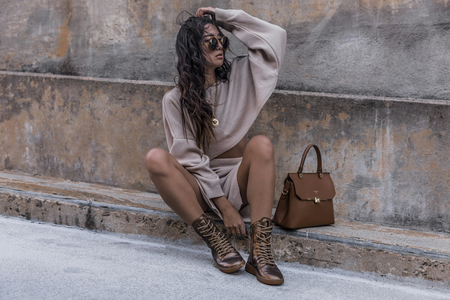 Femme assise portant un sac à main marron dans une tenue décontractée.