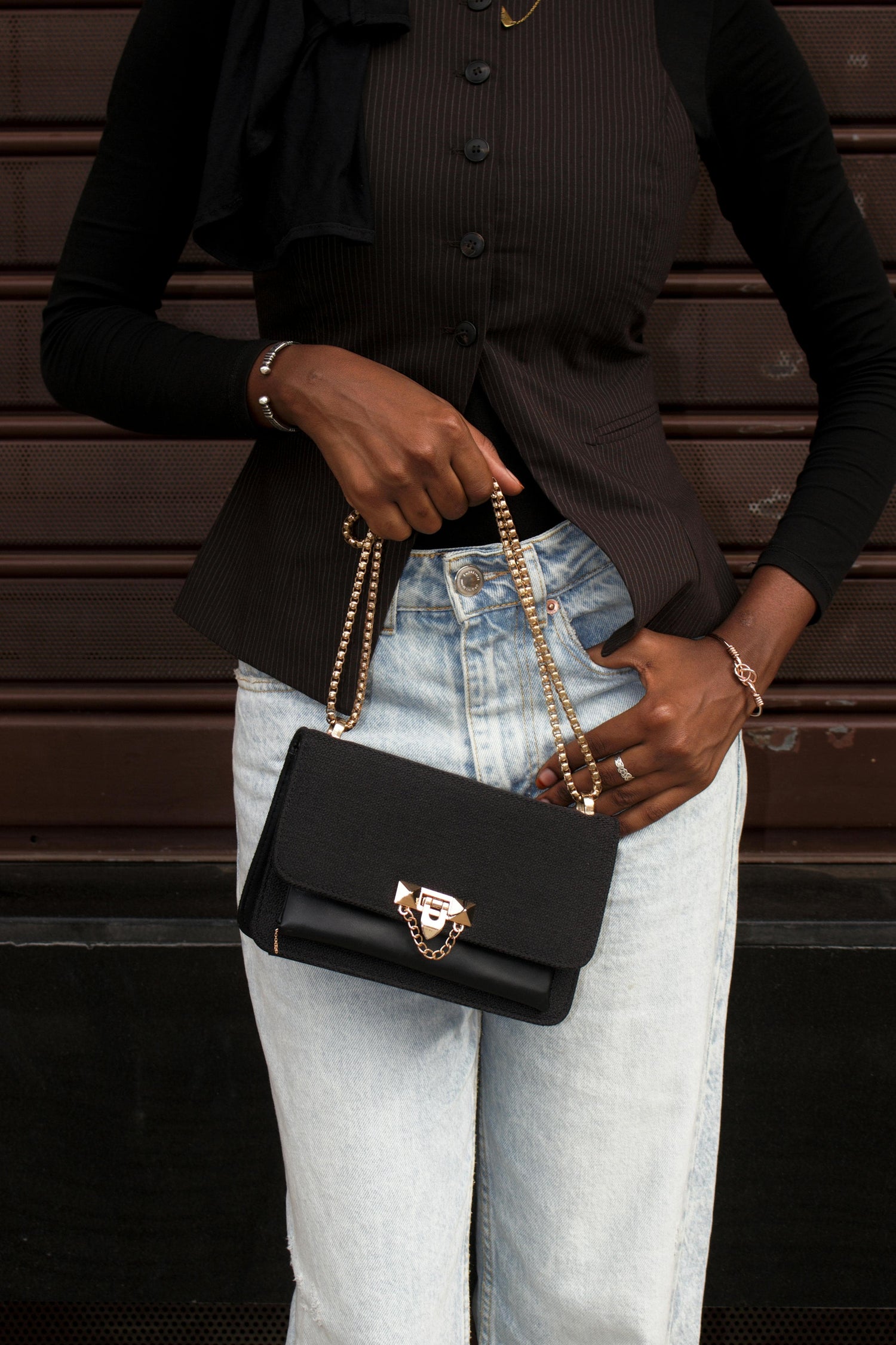 Femme portant un sac à main noir avec chaîne dorée dans une tenue élégante et décontractée.