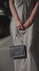 Femme portant un sac à main noir élégant avec bandoulière dans une tenue minimaliste.